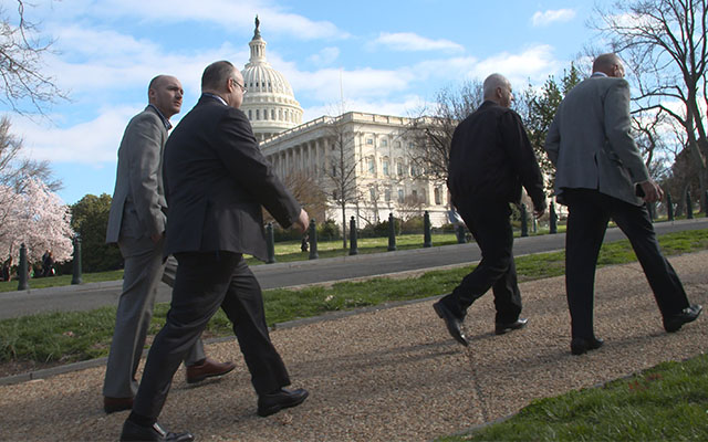 Men in suits walking in front of the US Capitol building